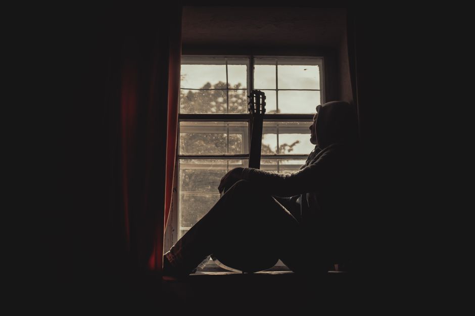 Person sitting quietly by a window in soft daylight, taking a slow breath during a moment of calm.